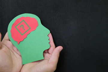 Human hands holding human head cutout with question mark in brain. Memory loss, uncertainty,...