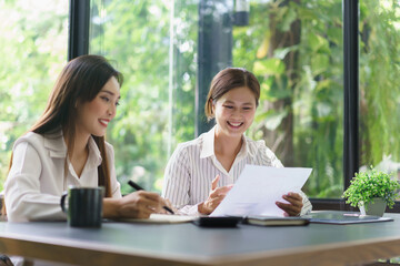 Obraz premium Coworker business concept, Two businesswoman reading financial chart document and taking notes