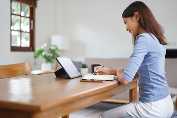 Work from home concept, Business women reads financial data on tablet and taking notes in notebook