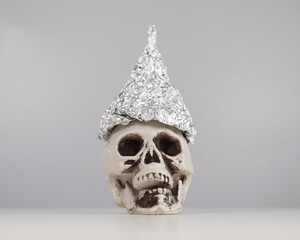 Plastic skull in a tinfoil cap on a white background. 