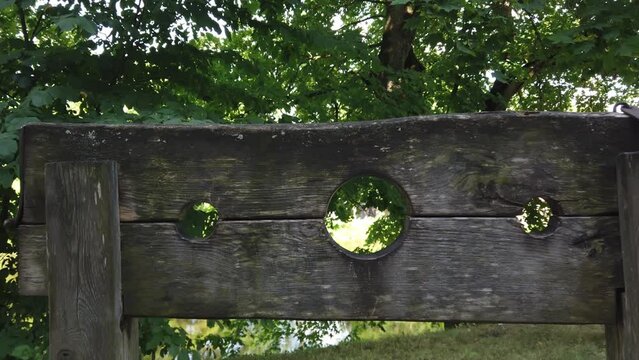 Wooden medieval device for punishment, torture, execution. Green foliage of trees in the background