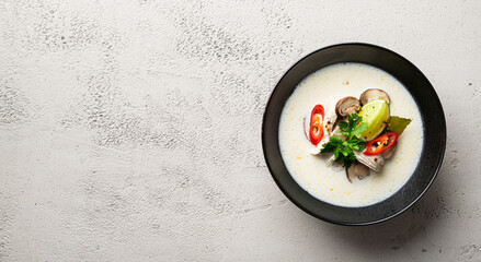 Tom Kha Gai, Thai Galangal chicken coconut soup in a black bowl on a concrete background, top view, copy space