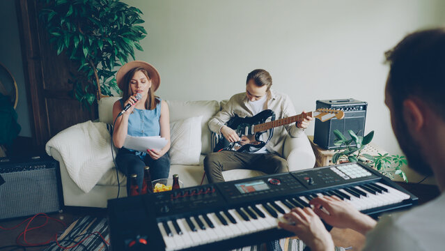 Group of creative friends guitarist, singer and keyboarder are playing musical instruments and singing during band practice in home studio. Music, friendship and people concept.