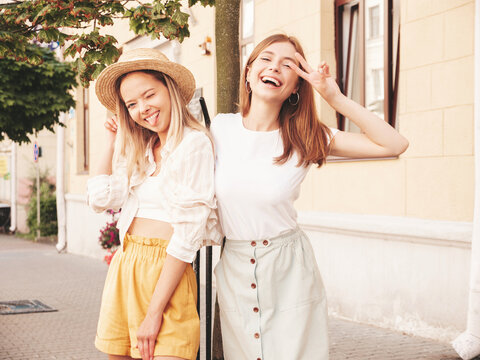 Two young beautiful smiling hipster female in trendy summer clothes.Sexy carefree women posing on the street background in hat. Positive pure models having fun at sunset, hugging