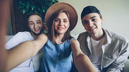 Point of view shot of creative funny friends holding camera and taking selfie, posing and...