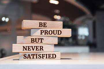 Wooden blocks with words 'Be proud but never satisfied'.