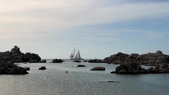 Double mast sailing ship crosses the scene at Cala della Chiesa on Lavezzi island in Corsica with people bathing, France