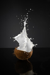 Half coconut with milk splash on black background	