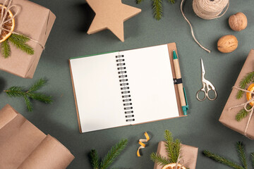Winter holiday mockup. Blank white notepad, boxes, craft paper, twine and natural decor for wrapping XMAS, New Year gifts on green background. Concept Zero waste Merry Christmas Mockup