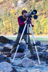 Full length shoit an attractive man in sportswear looking through telescope on bank of mountain rive