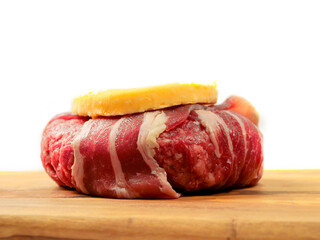 Luxury beef burger wrapped in bacon or rasher and portion of cheese on top on white background and wooden board. High quality product for barbecue or grill. Meat industry. Food supply.