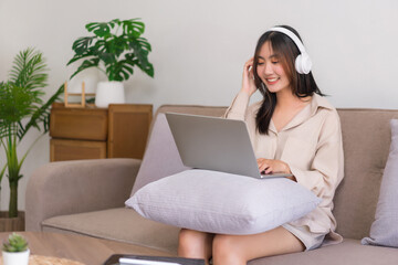 Concept of activity in living room, Asian woman is wearing headphone and listening music on laptop
