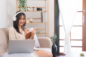 Lifestyle at home concept, Asian woman is taking notes on notebook while learning lesson online