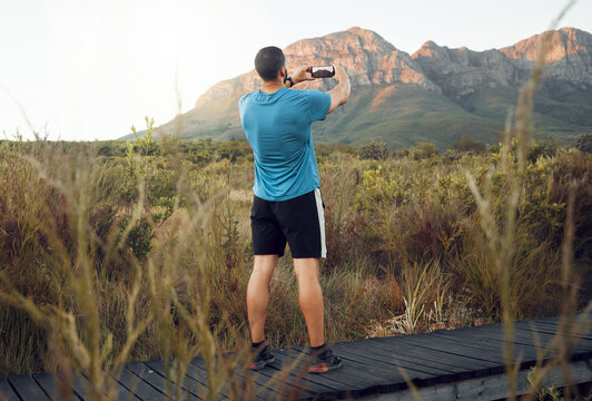 Phone, nature and fitness with a man taking a photograph while out for a sports run in the wilderness with a view. Exercise, training and workout with a picture of the mountain taken by male athlete