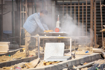 A worker wearing gloves uses an angle grinder to cut porcelain stoneware tiles, highly skilled...