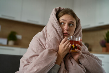 Caucasian woman sitting under the duvet with tea at home