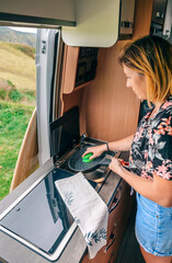 Young woman cleaning pan with sponge after eating in a camper van sink