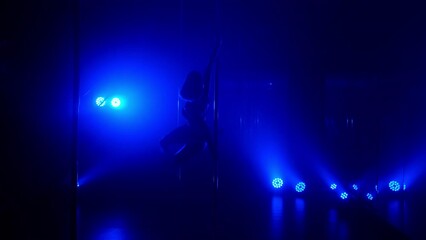 Slim woman performing poledance tricks sensually in spotlights. Sexy lady making moves upside down in night club. Young blonde dancer doing twine on pylon illuminated soft nightclub backlight.