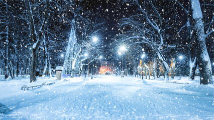 Snowfall in a winter park at night with christmas decorations, lights, pavement covered with snow...