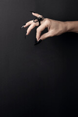Hand with long black nails and spider ring on a black background. Happy Halloween holiday concept