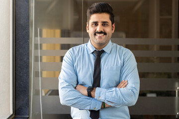 Businessman portrait. Happy confident young businessman standing arms crossed, smiling, looking at camera.