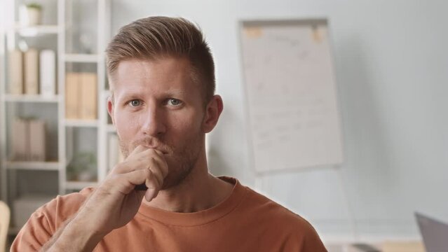 Medium closeup portrait of young Caucasian man smoking electronic cigarette and smiling at camera in office