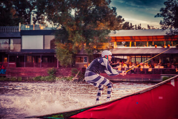 A guy in a yak suit at sunset jumps from a springboard on a wakeboard in an extreme park in Kiev....