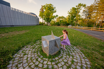 Girl look at sun watches stone cube in planetarium outdoor.