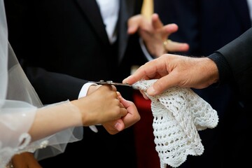 Hands of the newlyweds and the priest's cross at the wedding in the Church