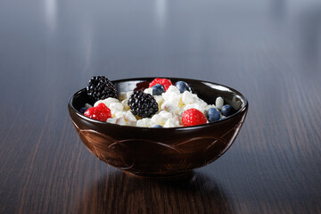 Russian grained cottage cheese with fresh raspberries and blueberries and blackberries in a clay bowl for a healthy breakfast. Close-up, selective focus.