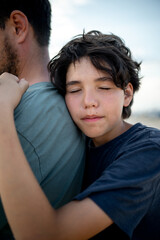 The teenage boy snuggles with tenderness to the strong shoulder of the father, the child seeks...