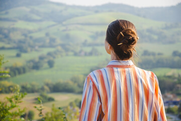 A woman with a chignon is looking at the Montefeltro hills, in the Marche Region of Italy, near Pesaro and Urbino during a nice sunny autumn afternoon - obrazy, fototapety, plakaty