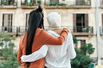Multi-ethnic female friends embracing each other while standing outdoors on the street.