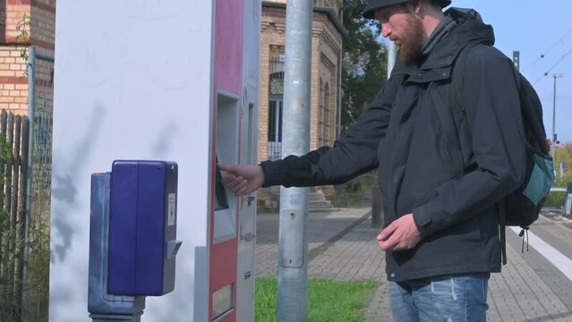 young man with a beard buys a ticket from a machine at a railway station