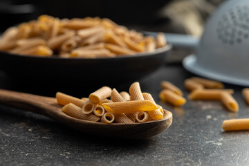 Uncooked whole grain pasta. Raw penne pasta on wooden spoon.