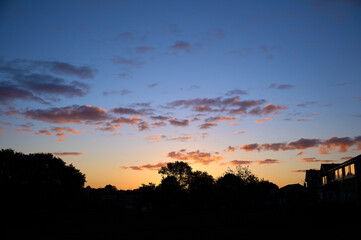 A blue and orange sky of a sunset and the silhouette of trees and homes in a small town in England UK.