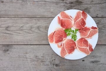 Raw Pork Slice in White Round Plate on old Wooden Table. Slide raw meat on the table decorated with parsley on a white plate