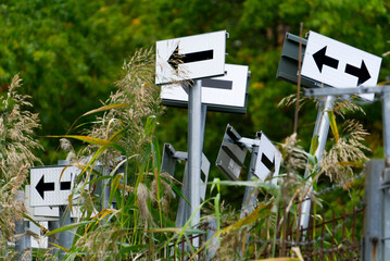 Signs with arrows behind a rusty fence by the forest