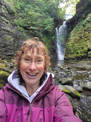 Wild swimming at Sgwd Einion Gam - one of the waterfalls in Waterfall Country on the river Neath near Pontneddfechan. Mature woman has wet hair and is wearing warm clothing to regain body temperature.