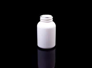 Medical pills in white jar on an isolated black background with reflection