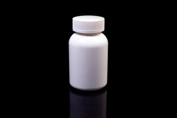 Medical pills in white jar on an isolated black background with reflection