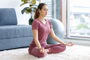 Foto op Aluminium Millennial Asian young healthy female housewife sitting on carpet floor in living room doing hobby yoga exercising with lotus pose position meditating alone for good body care health and wellness © Bangkok Click Studio
