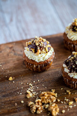 Tasty chocolate muffin with creme mascarpone and chocolate on top, covered with nuts. Placed on wooden desk. Sweet fresh and homemade cupcake.