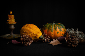 Close-up of pumpkins with autumn leaves and lit candle, on tablecloth and black background, horizontal, with copy space
