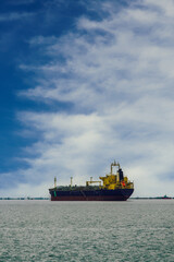 Day view of moored cargo ship at a calm sea against blue sky with dense white clouds.