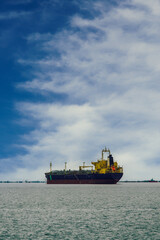 Naklejka premium Day view of moored cargo ship at a calm sea against blue sky with dense white clouds.