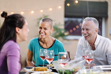 Happy woman with shaved hair enjoying dinner with family friends cheering having fun at dinner