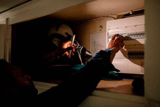 Man turning on switch from fuse box using smart phone torch during blackout