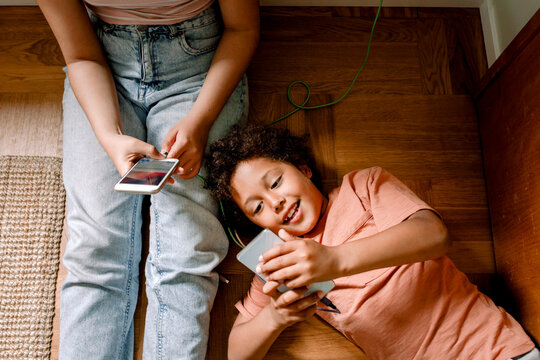 Smiling boy using smart phone with sister while lying down on floor at home