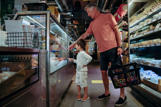 Senior man showing food to grandson in display while shopping at supermarket